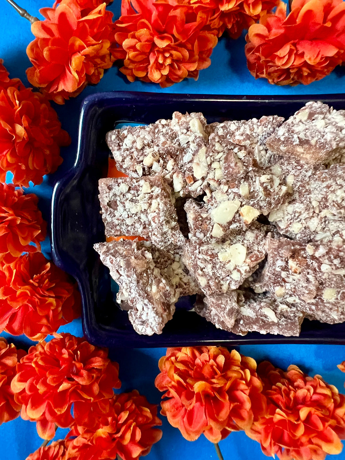 tray of milk chocolate toffee on a blue background surrounded by orange flowers