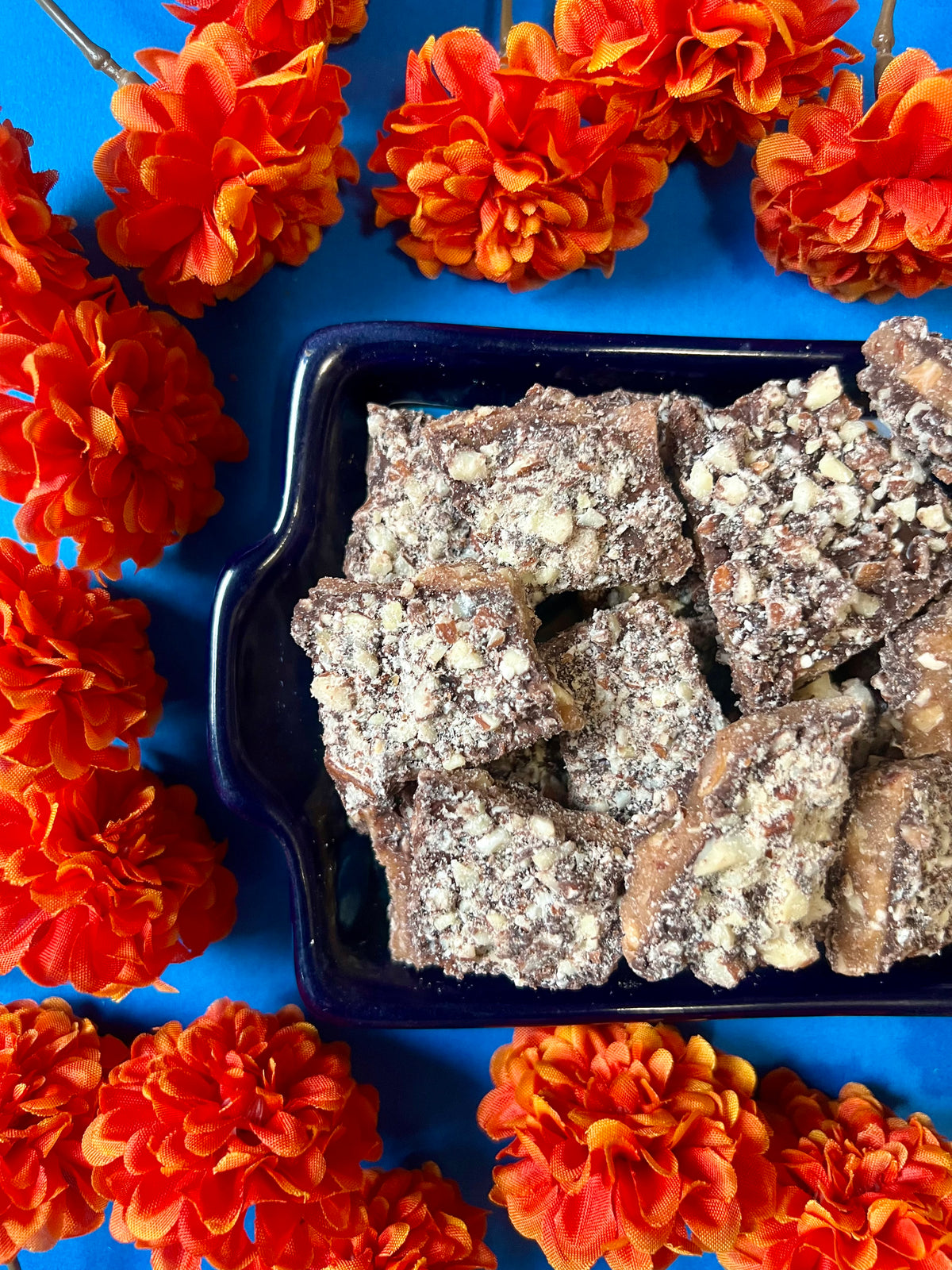 tray of dark chocolate toffee on a blue background surrounded by orange flowers