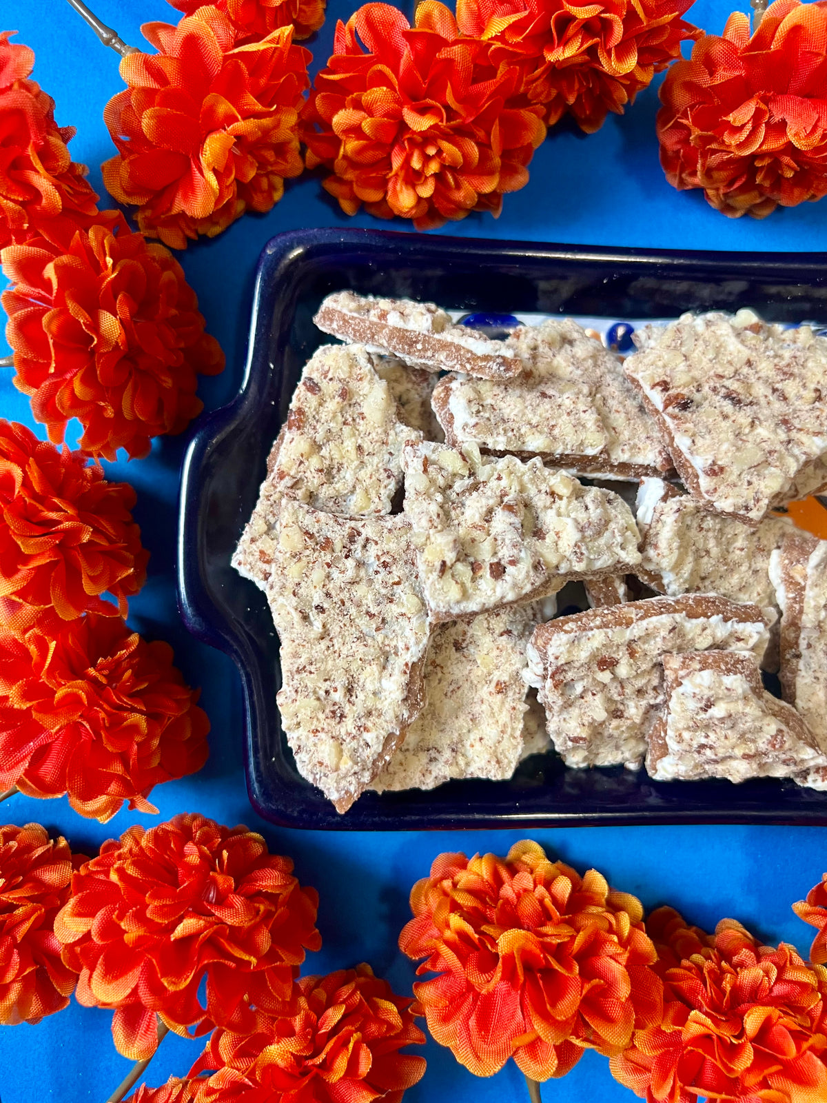 tray of white chocolate toffee on a blue background surrounded by orange flowers